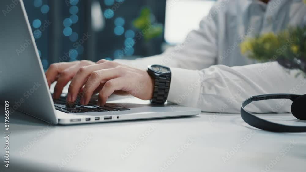 Shooting of male hand in white classic shirt with black prestigious man's wrist watch. Editorial concept. Young Caucasian man sitting at laptop, typing on keyboard. Blurred background. Office, indoors