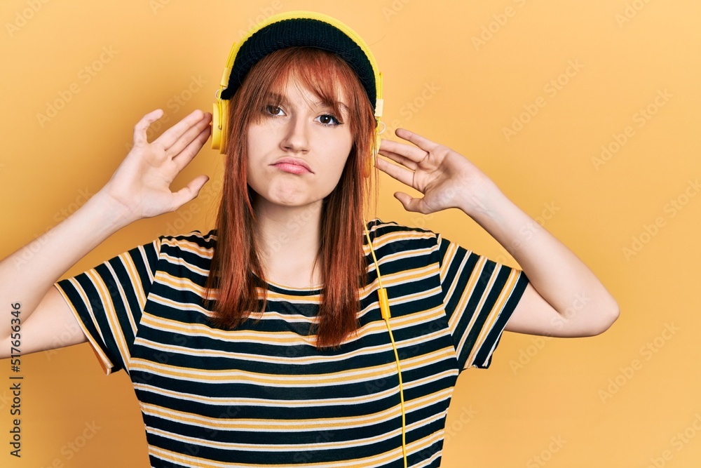 Fototapeta premium Redhead young woman listening to music using headphones depressed and worry for distress, crying angry and afraid. sad expression.