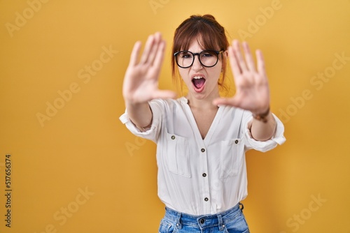 Young beautiful woman wearing casual shirt over yellow background doing stop gesture with hands palms, angry and frustration expression