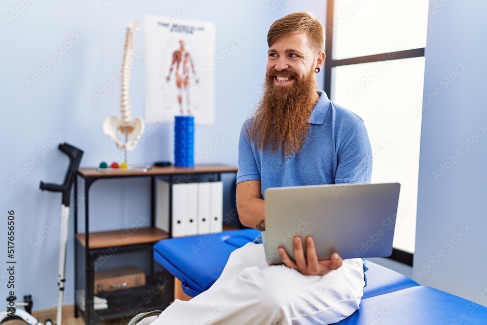 Young redhead man wearing physiotherapist uniform using laptop at physiotherapy clinic Young redhead man wearing physiotherapist uniform using laptop at physiotherapy clinic