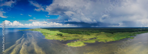 Aerial panoramic view to the shallow coastal sea with sandbanks, green semi.natural grazed coastal meadow and inland marshes with passing rain front background. Luitemaa nature reserve, Estonia.