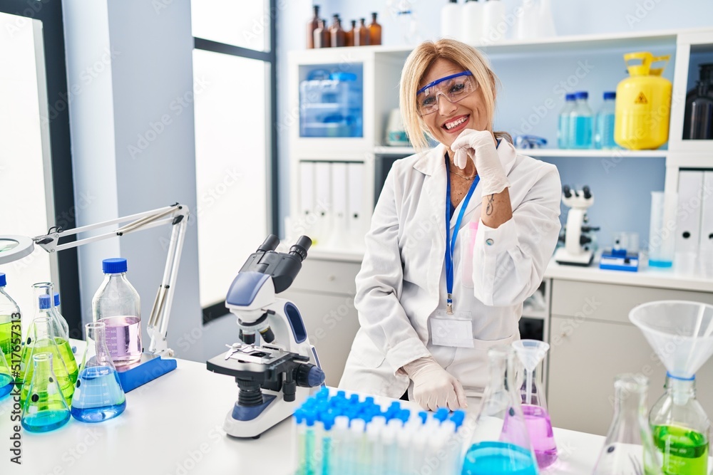 Middle age blonde woman working at scientist laboratory with hand on chin thinking about question, pensive expression. smiling and thoughtful face. doubt concept. Middle age blonde woman working at scientist laboratory with hand on chin thinking about question, pensive expression. smiling and thoughtful face. doubt concept.