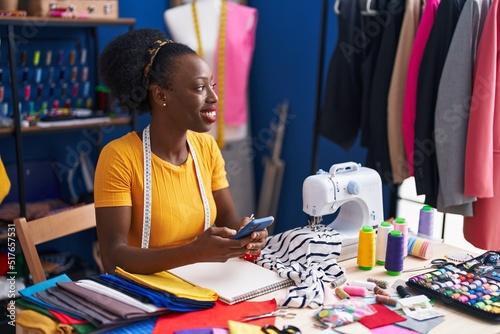 African american woman tailor smiling confident using smartphone at sewing studio photo