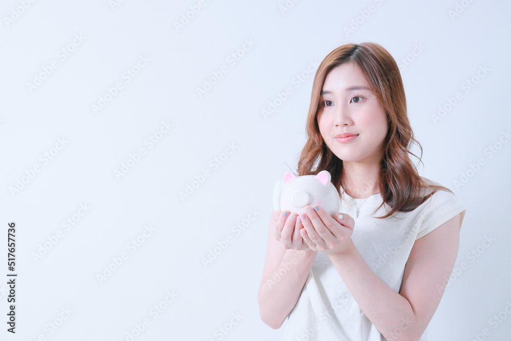 貯金箱を手のひらに乗せ遠くを見つめる女性 貯金箱を手のひらに乗せ遠くを見つめる女性