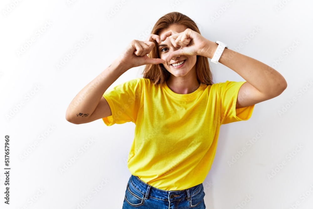 Young brunette woman standing over isolated background doing heart shape with hand and fingers smiling looking through sign Young brunette woman standing over isolated background doing heart shape with hand and fingers smiling looking through sign