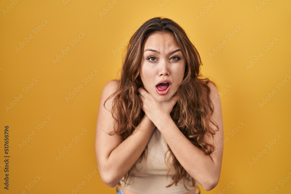 Young hispanic woman standing over yellow background shouting and suffocate because painful strangle. health problem. asphyxiate and suicide concept. Young hispanic woman standing over yellow background shouting and suffocate because painful strangle. health problem. asphyxiate and suicide concept.
