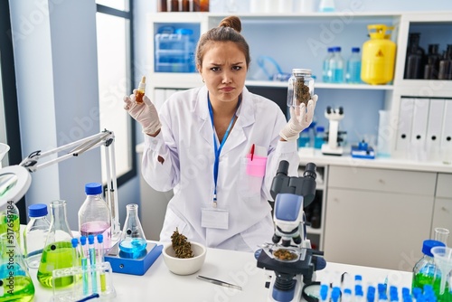 Fototapeta Naklejka Na Ścianę i Meble -  Young hispanic woman doing weed oil extraction at laboratory skeptic and nervous, frowning upset because of problem. negative person.