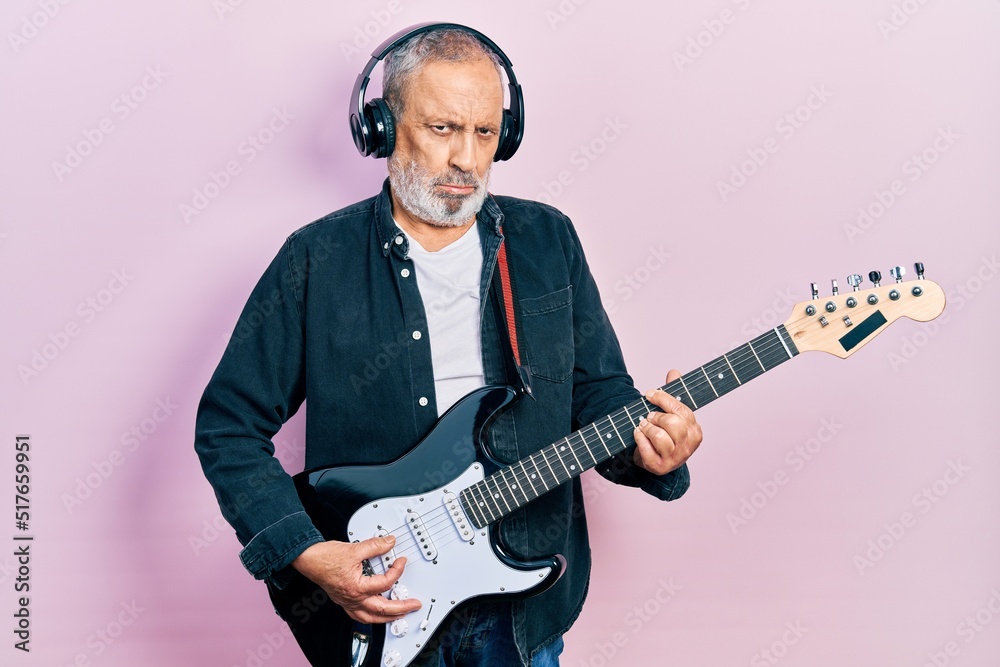 Obraz premium Handsome senior man with beard playing electric guitar depressed and worry for distress, crying angry and afraid. sad expression.