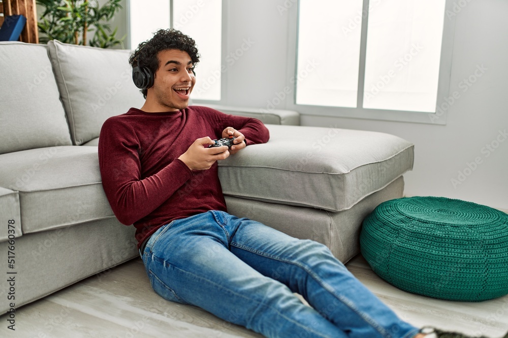 Obraz premium Young hispanic man playing video game sitting on the floor at home.