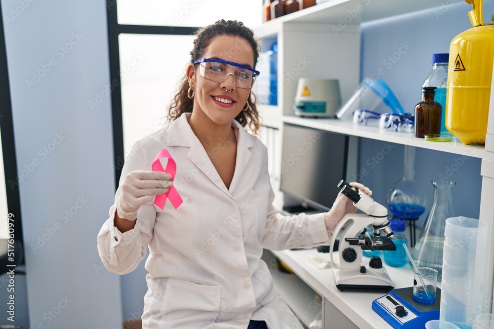 Young hispanic woman working at scientist laboratory looking for breast cancer cure smiling with a happy and cool smile on face. showing teeth.