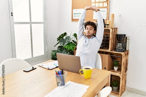 Young hispanic businessman relaxed stretching arms at the office.