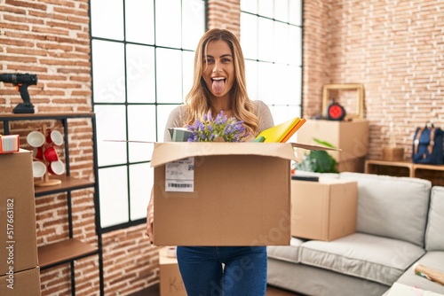 Young blonde woman moving to a new home holding cardboard box sticking tongue out happy with funny expression. © Krakenimages.com