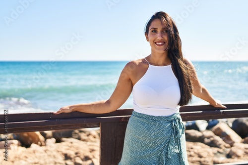 Stampa su tela Young hispanic woman smiling confident leaning on balustrade at seaside