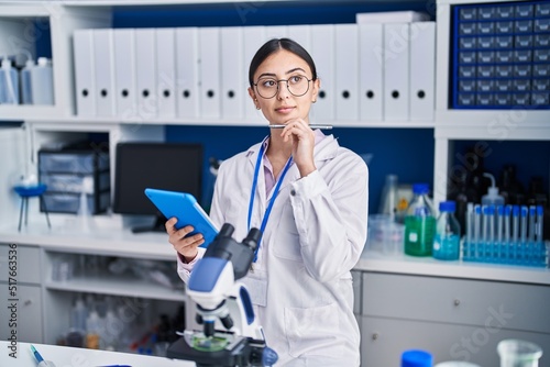 Young hispanic woman scientist using touchpad working at laboratory