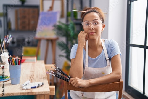 Young woman artist sitting on chair holding paintbrush at art studio