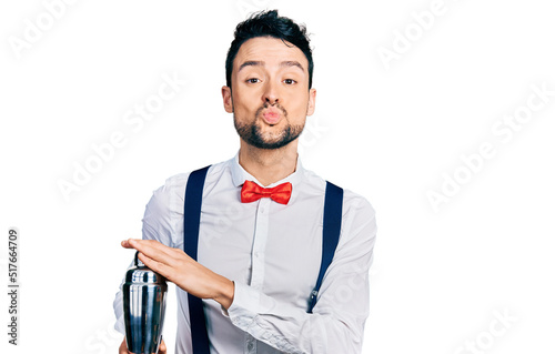 Hispanic man with beard preparing cocktail mixing drink with shaker looking at the camera blowing a kiss being lovely and sexy. love expression.