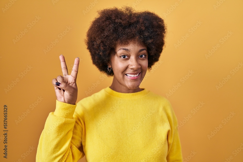 Young african american woman standing over yellow background showing and pointing up with fingers number two while smiling confident and happy. Young african american woman standing over yellow background showing and pointing up with fingers number two while smiling confident and happy.