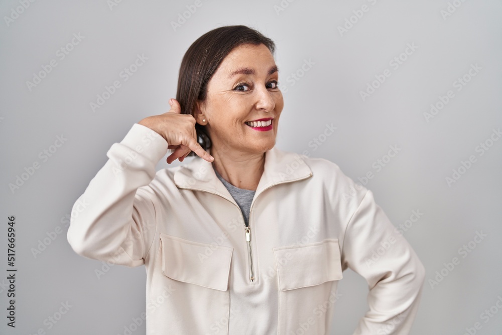 Middle age hispanic woman standing over isolated background smiling doing phone gesture with hand and fingers like talking on the telephone. communicating concepts. Middle age hispanic woman standing over isolated background smiling doing phone gesture with hand and fingers like talking on the telephone. communicating concepts.
