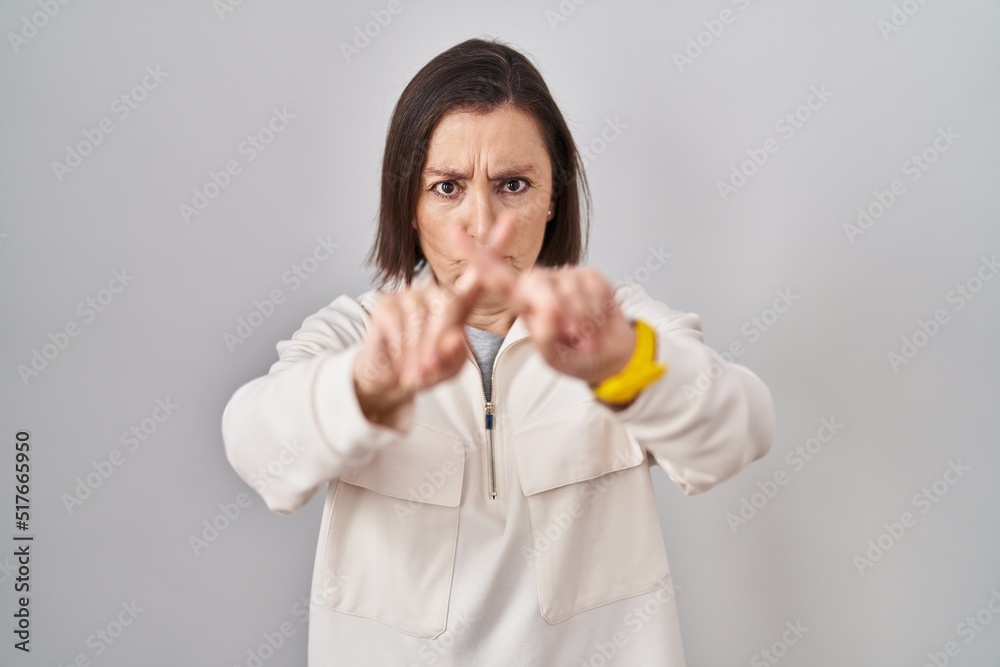 Middle age hispanic woman standing over isolated background rejection expression crossing fingers doing negative sign