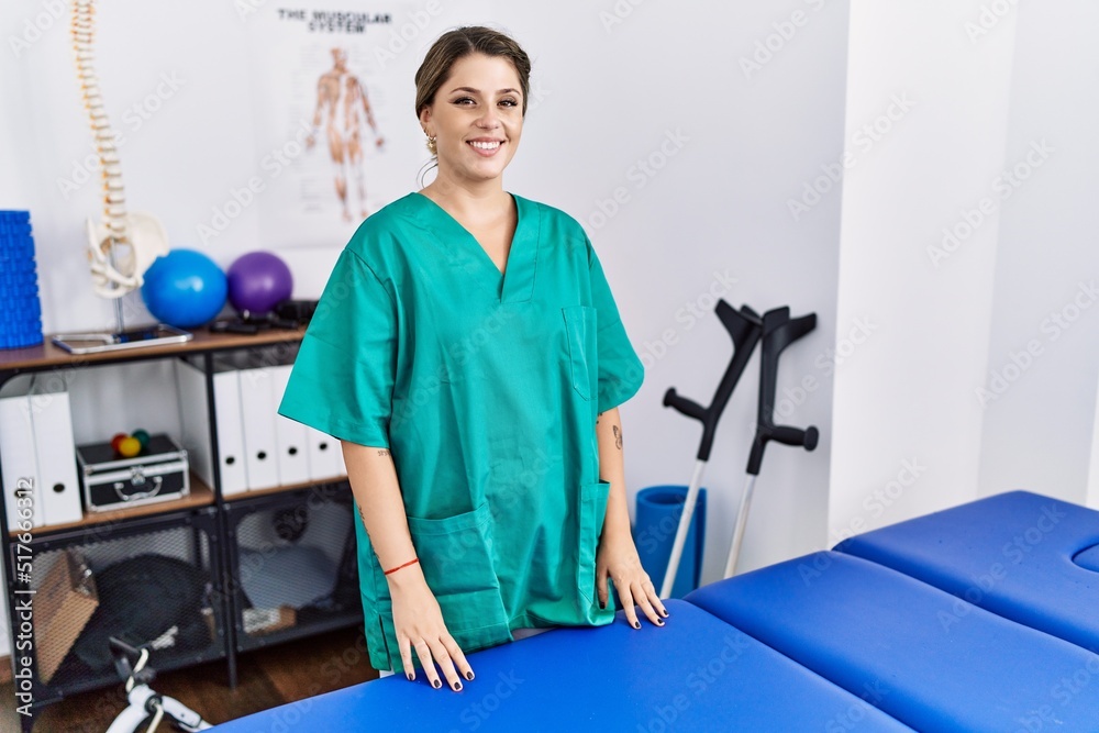 Young hispanic woman wearing physiotherapist uniform standing at clinic with a happy and cool smile on face. lucky person. Young hispanic woman wearing physiotherapist uniform standing at clinic with a happy and cool smile on face. lucky person.
