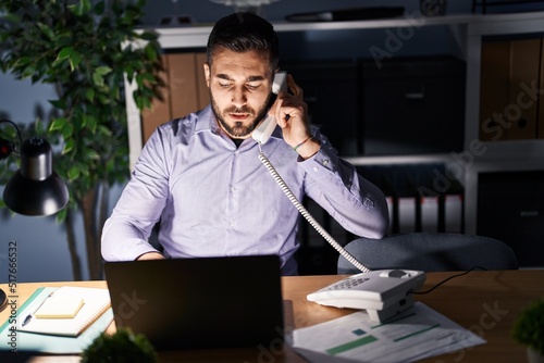 Young hispanic man business worker talking on the telephone working overtime at office