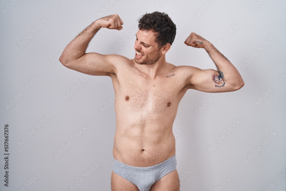 Young hispanic man standing shirtless wearing underware showing arms muscles smiling proud. fitness concept.