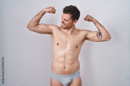 Young hispanic man standing shirtless wearing underware showing arms muscles smiling proud. fitness concept. photo