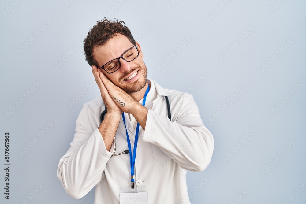 Young hispanic man wearing doctor uniform and stethoscope sleeping tired dreaming and posing with hands together while smiling with closed eyes. Young hispanic man wearing doctor uniform and stethoscope sleeping tired dreaming and posing with hands together while smiling with closed eyes.