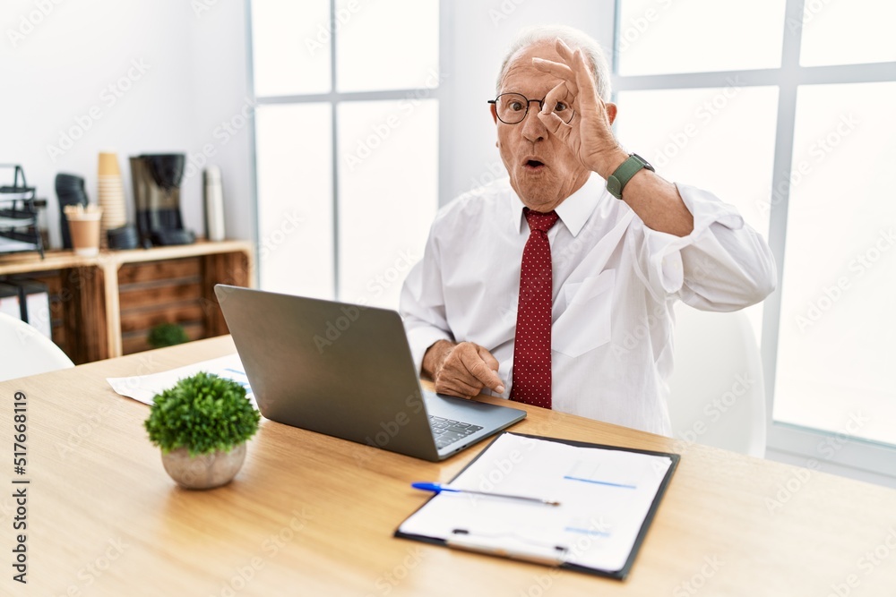 Senior man working at the office using computer laptop doing ok gesture shocked with surprised face, eye looking through fingers. unbelieving expression. Senior man working at the office using computer laptop doing ok gesture shocked with surprised face, eye looking through fingers. unbelieving expression.