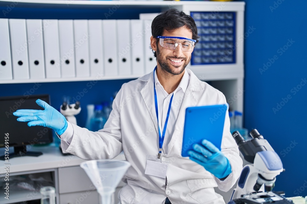 Handsome latin man working at scientist laboratory using tablet celebrating achievement with happy smile and winner expression with raised hand Handsome latin man working at scientist laboratory using tablet celebrating achievement with happy smile and winner expression with raised hand