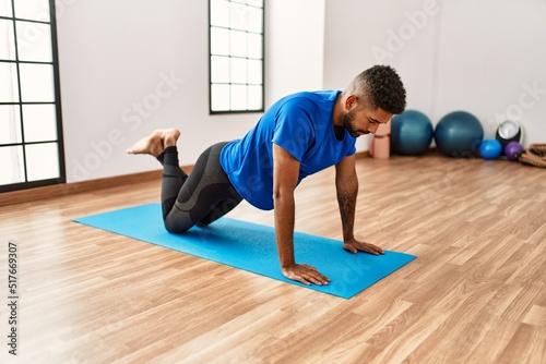 Handsome hispanic man doing exercise and stretching on yoga mat, practicing flexibility and training at the gym