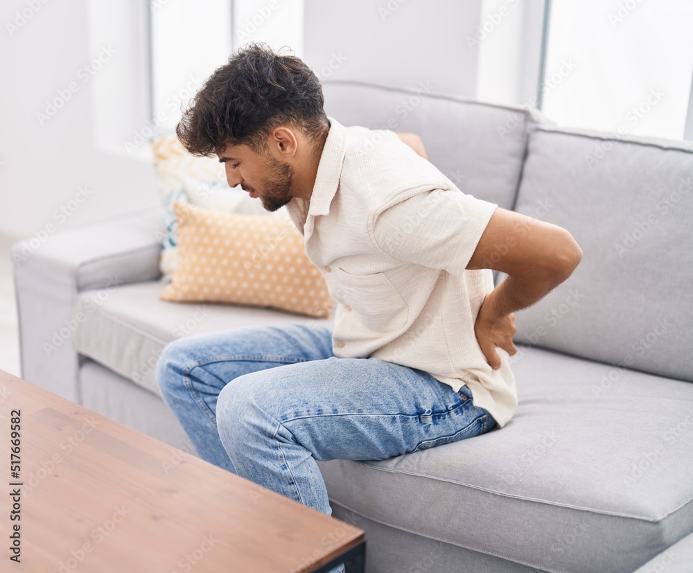 Young arab man suffering for backache sitting on sofa at home Young arab man suffering for backache sitting on sofa at home