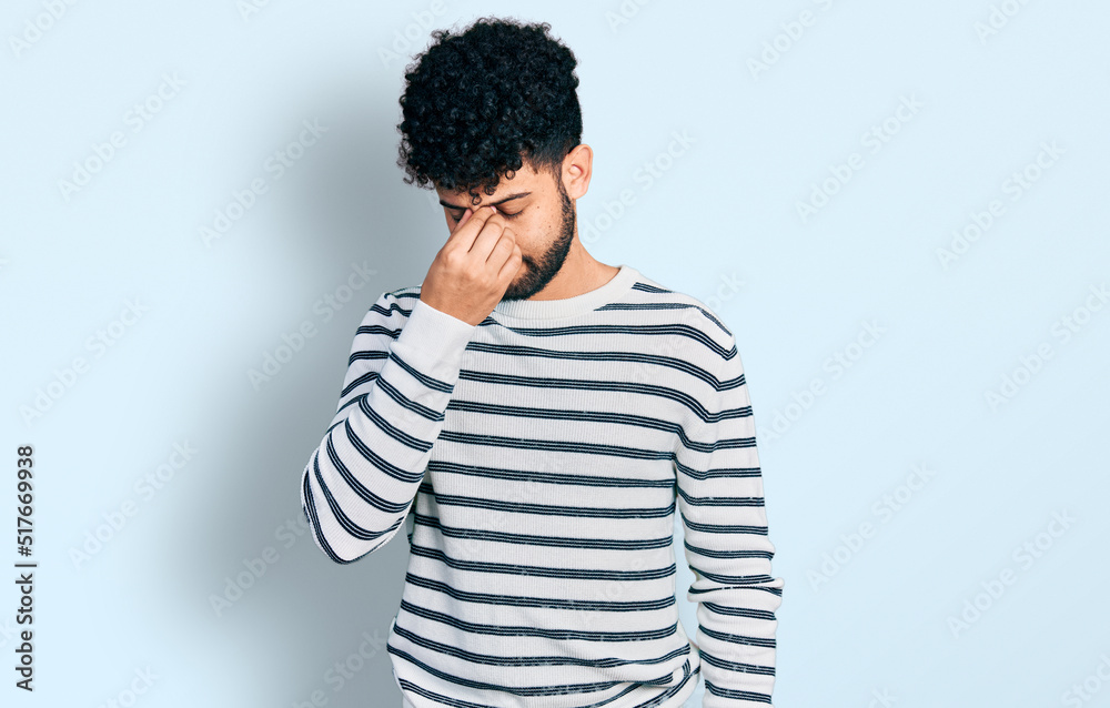 Young arab man with beard wearing casual striped sweater tired rubbing nose and eyes feeling fatigue and headache. stress and frustration concept. Young arab man with beard wearing casual striped sweater tired rubbing nose and eyes feeling fatigue and headache. stress and frustration concept.
