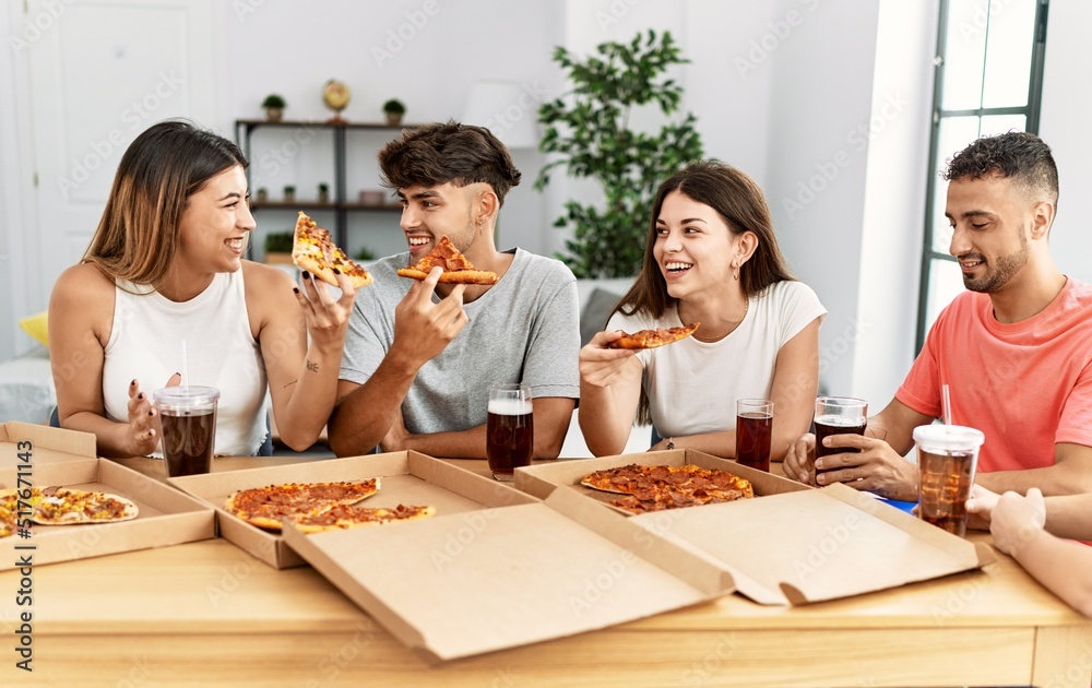 Group of young people smiling happy eating italian pizza sitting on the table at home Group of young people smiling happy eating italian pizza sitting on the table at home