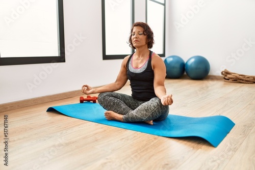 Middle age hispanic sporty woman concentrate training yoga at sport center.