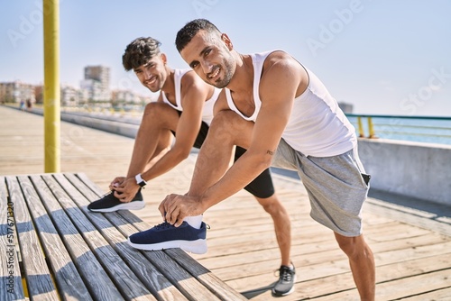 Two hispanic men couple smiling confident tying shoelace at seaside