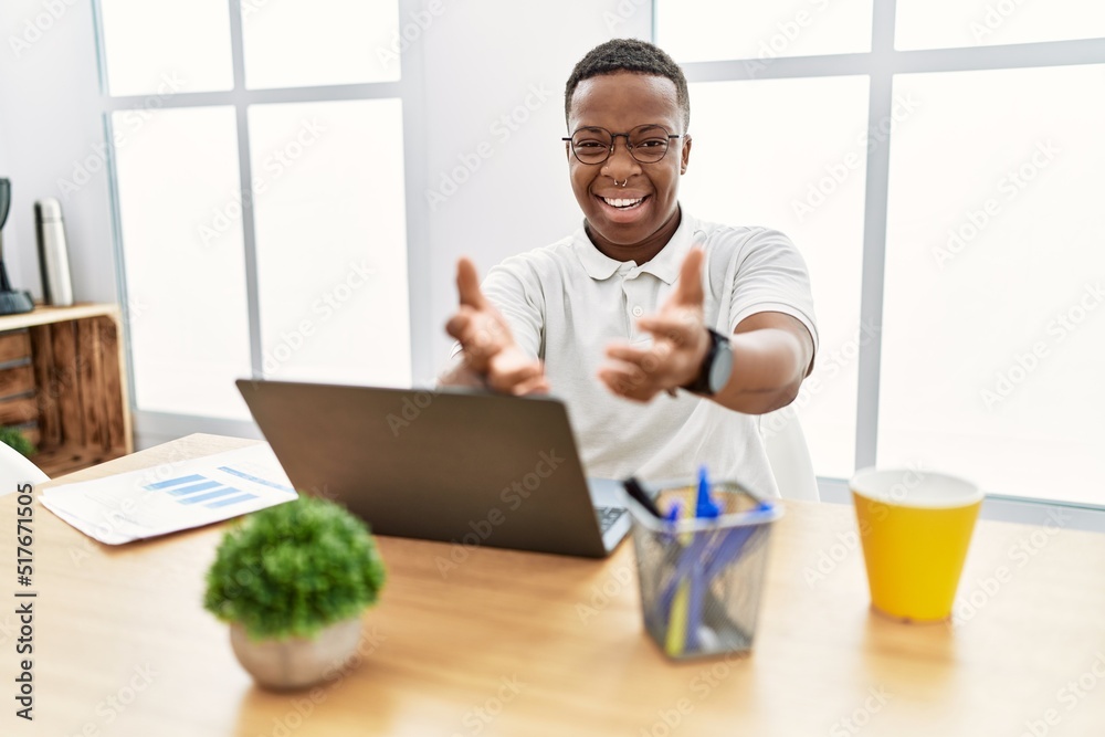 Young african man working at the office using computer laptop smiling with hands palms together receiving or giving gesture. hold and protection Young african man working at the office using computer laptop smiling with hands palms together receiving or giving gesture. hold and protection