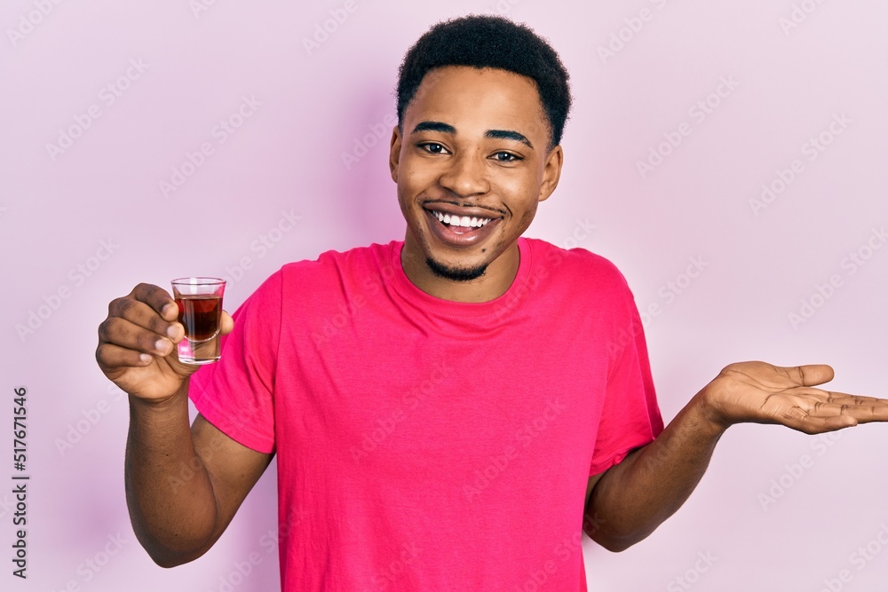 Young african american man drinking whiskey shot celebrating achievement with happy smile and winner expression with raised hand Young african american man drinking whiskey shot celebrating achievement with happy smile and winner expression with raised hand