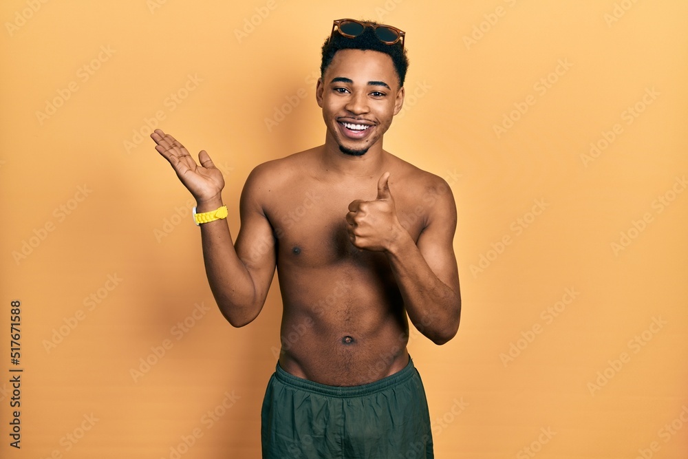 Young african american man wearing swimwear and swimmer glasses showing palm hand and doing ok gesture with thumbs up, smiling happy and cheerful Young african american man wearing swimwear and swimmer glasses showing palm hand and doing ok gesture with thumbs up, smiling happy and cheerful