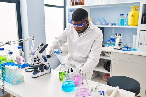 Young african american man wearing scientist uniform measuring liquid at laboratory