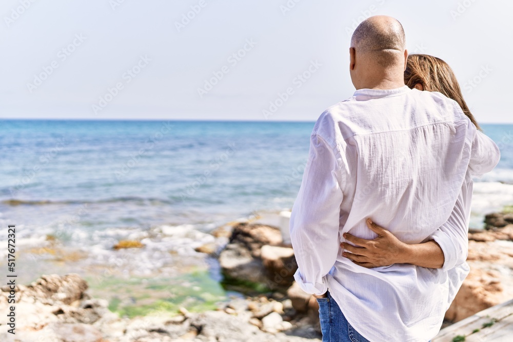 Middle age hispanic couple of husband and wife together walking by the beach on a sunny day. Hugging in love on vacation to the seaside. Middle age hispanic couple of husband and wife together walking by the beach on a sunny day. Hugging in love on vacation to the seaside.