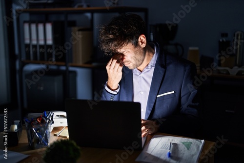 Hispanic young man working at the office at night tired rubbing nose and eyes feeling fatigue and headache. stress and frustration concept.