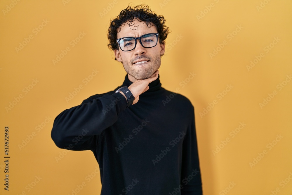 Hispanic man standing over yellow background cutting throat with hand as knife, threaten aggression with furious violence Hispanic man standing over yellow background cutting throat with hand as knife, threaten aggression with furious violence