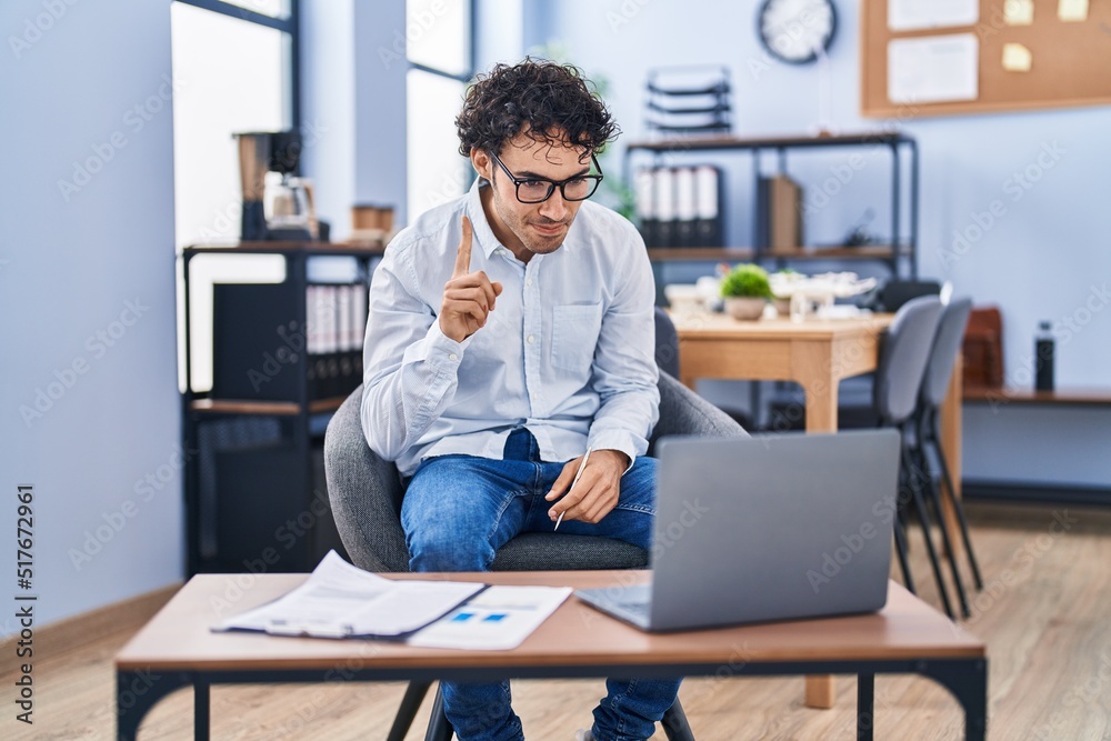 Hispanic man doing video call waving to laptop smiling with an idea or question pointing finger with happy face, number one Hispanic man doing video call waving to laptop smiling with an idea or question pointing finger with happy face, number one
