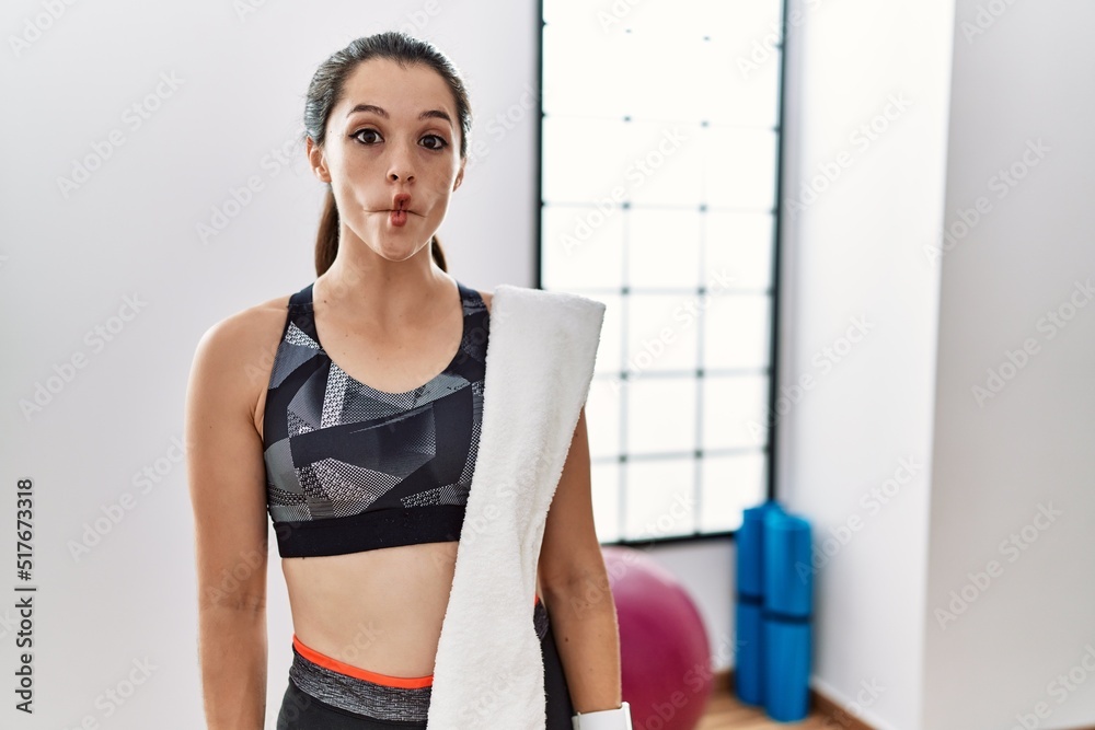 Young brunette woman wearing sportswear and towel at the gym making fish face with lips, crazy and comical gesture. funny expression.