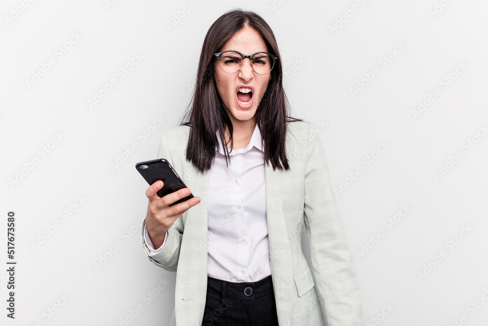 Young business caucasian woman holding mobile phone isolated on white background screaming very angry and aggressive. Young business caucasian woman holding mobile phone isolated on white background screaming very angry and aggressive.