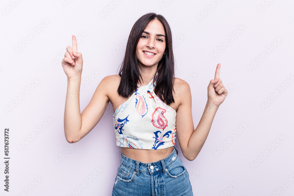 Young caucasian woman isolated on pink background indicates with both fore fingers up showing a blank space. Young caucasian woman isolated on pink background indicates with both fore fingers up showing a blank space.
