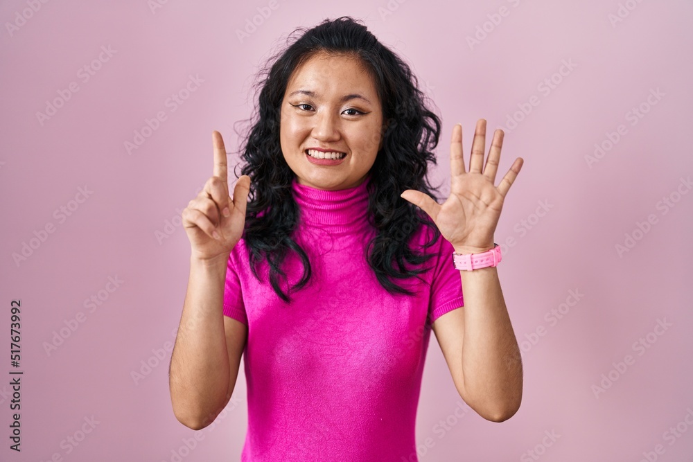 Young asian woman standing over pink background showing and pointing up with fingers number seven while smiling confident and happy. Young asian woman standing over pink background showing and pointing up with fingers number seven while smiling confident and happy.