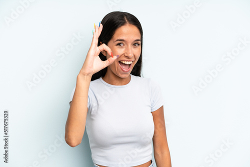 hispanic pretty woman feeling successful and satisfied, smiling with mouth wide open, making okay sign with hand