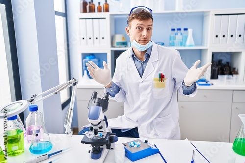 Caucasian man working at scientist laboratory shouting and screaming loud to side with hand on mouth. communication concept.